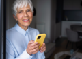 Idosa confiante com smartphone amarelo em casa bem iluminada.