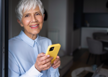Idosa confiante com smartphone amarelo em casa bem iluminada.