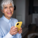 Idosa confiante com smartphone amarelo em casa bem iluminada.