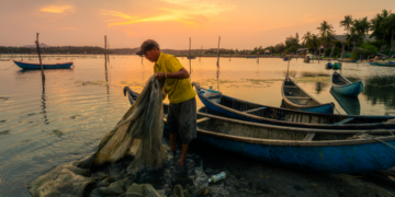 Pescador recolhendo rede ao pôr do sol.