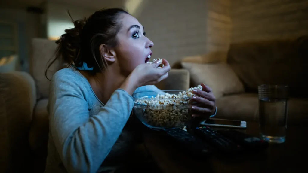 Jovem comendo pipoca e concentrada assistindo.