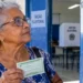 Eleitora idosa segura título de eleitor em frente a local de votação nas eleições.