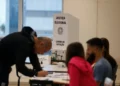 Pessoa votando em seção eleitoral durante as eleições, com destaque para a cabine de votação da Justiça Eleitoral.