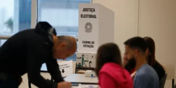 Pessoa votando em seção eleitoral durante as eleições, com destaque para a cabine de votação da Justiça Eleitoral.