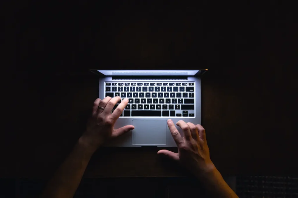 Pessoa utiliza notebook em ambiente escuro, representando riscos de golpes digitais contra idosos.