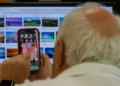 Idoso acessa redes sociais pelo celular enquanto utiliza computador.