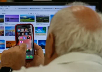 Idoso acessa redes sociais pelo celular enquanto utiliza computador.