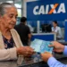 Aposentada recebe dinheiro em agência da Caixa, representando o pagamento do benefício do INSS referente ao mês de setembro.
