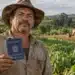 Agricultor brasileiro segurando carteira de trabalho em uma plantação, com trator ao fundo, representando a aposentadoria rural do INSS.