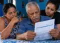 Idoso acompanhado de duas familiares analisa uma conta de água, representando o desconto de 50% na tarifa para famílias com beneficiários do BPC.