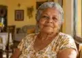 Mulher idosa de cabelos grisalhos, sentada próxima a uma janela em ambiente familiar, representando a valorização da pessoa idosa durante o Outubro Prata.