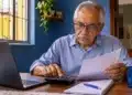 Idoso aposentado utiliza calculadora e analisa documentos financeiros, representando o planejamento de renda e gastos após a aposentadoria.