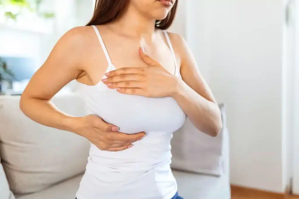 Mulher realiza a palpação das mamas com as duas mãos, representando a observação das possíveis alterações que podem indicar sinais de alerta para o câncer de mama.