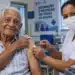 Idoso com mais de 85 anos recebe vacina no braço aplicada por profissional de enfermagem em unidade de saúde, ilustrando a vacinação contra pneumonia na Baixada Santista.